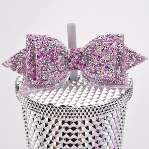 Close-up of sparkling pink and silver glitter bow straw toppers on a studded tumbler cup