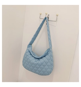 Detail of blue quilted nylon hobo bag with adjustable strap on white wall