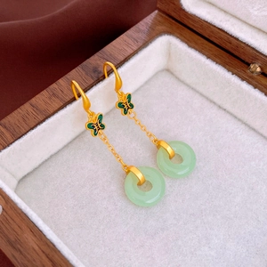 Détail de boucles d'oreilles dorées avec papillon vert et pendentif en jade