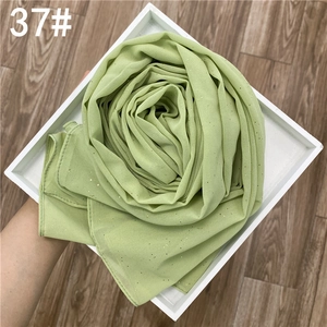 Détail du tissu de l'écharpe en mousseline vert clair avec paillettes dorées pliées
