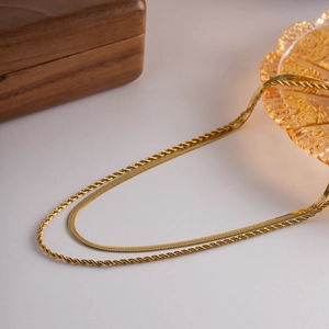 Detail view of gold layered snake and twisted rope necklaces on a minimalist background