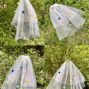 Detail view of double-layer white wedding veil featuring vibrant colorful pom pom accents