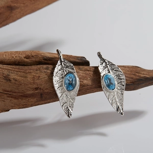 Leaf design S925 silver pendant with blue topaz gemstones on a wooden background