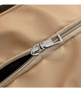 Close-up of smooth silver metal zipper and durable nylon fabric on a khaki tote bag