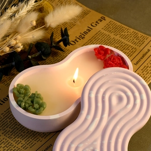 Pink peanut-shaped candle jar with wavy lid and wax floral accents on a vintage table