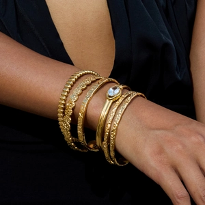 Dettaglio di bracciali placcati in oro a strati con intarsio di zirconi sul polso della modella