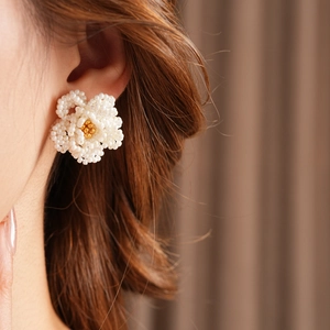 Macro shot of a pearl-woven camellia flower earring with a golden bead accent