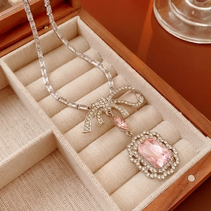 Détail macro d'un collier nœud avec gemme rose dans un coffret à bijoux en velours beige