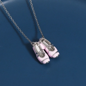 Close-up of pink enamel ballet slipper pendant necklace on blue ceramic plate