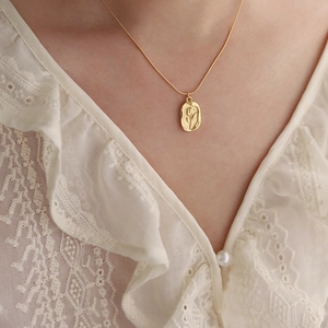 Gros plan d'un collier pendentif tulipe doré en relief sur chemise en dentelle