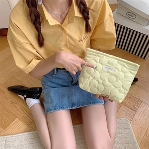 Detail of floral quilted cosmetic bag in pale yellow held by hand for scale