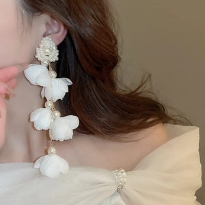 Detailed close-up of a long floral earring with white petals and pearls worn by a model