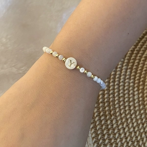 Close-up of beaded bracelet featuring white pearls and a golden initial Y charm