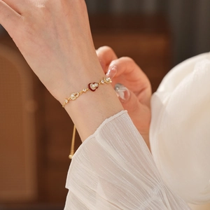Detail of a gold heart bracelet with pearls and red enamel on a woman's wrist