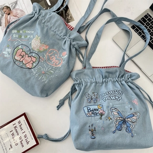 Detail of blue denim tote bags featuring butterfly embroidery and drawstring closure