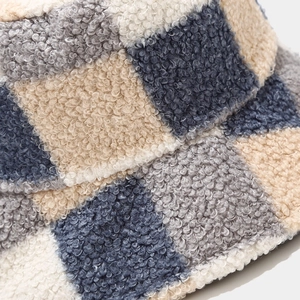 Close-up of plush plaid bucket hat fabric showing soft beige, grey and navy blue textures