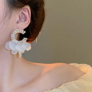 Detail of C-shaped gold earrings featuring zircon inlay and white translucent petals