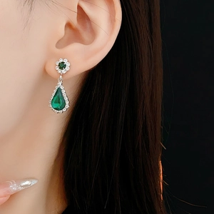 Close-up of green teardrop earrings with silver flower studs on a model with black background