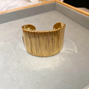 Detail of golden twisted wire cuff bracelet on a soft grey velvet jewelry display tray