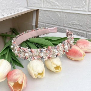 Pink woven fabric headband with faux pearls and gold thread on a clean white desk
