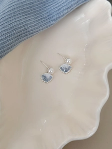 Macro detail of silver shell earrings with pearls on a white ceramic display tray