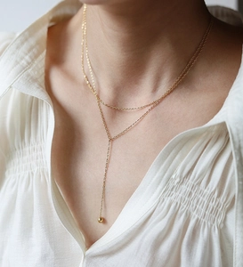 Detail of a layered Y-shaped gold necklace with round beads on a white pleated shirt