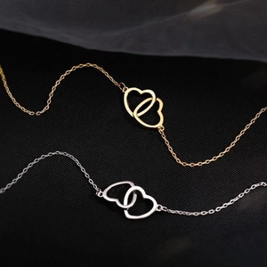 Elegant gold and silver interlocking heart necklaces displayed on a black fabric background