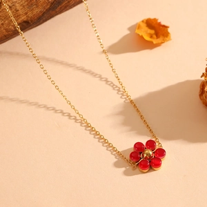 Detail of gold floral necklace with red gemstones on a minimalist textured surface