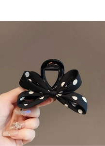 Détail d'une pince à cheveux à nœud en satin à pois noirs et blancs tenue à la main