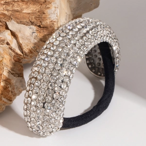 Close-up of sparkling silver rhinestone hair tie with thick black elastic band on stone
