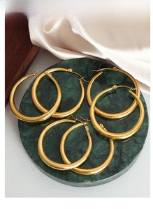 Detail of large chunky gold hoop earrings displayed on a green marble tray with silk