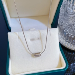 Dettaglio di un ciondolo a fagiolo in argento minimalista su una catena a serpente