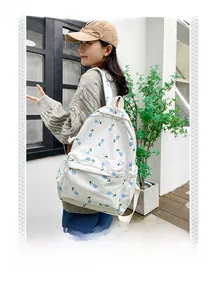 Detail of white floral backpack with blue tulip print worn by model against a clean wall