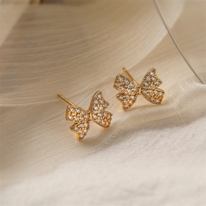 Close-up of gold 18K plated bow earrings with sparkling crystal pave on beige fabric
