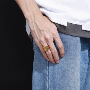 Primo piano di un anello quadrato dorato lucido indossato sulla mano su sfondo scuro
