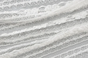 Dettaglio del tessuto in pizzo bianco semitrasparente con trama floreale delicata