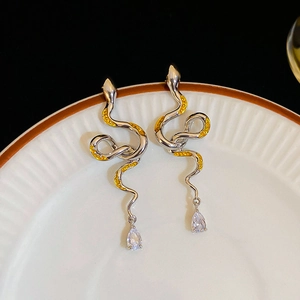 Macro detail of snake-shaped silver earrings with yellow enamel and teardrop crystals