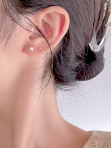 Close-up of a silver floral pearl earring and ball stud worn on a female ear
