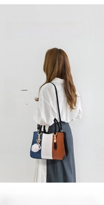 Detail of a three-color leather tote bag featuring a decorative pompom and bow charm