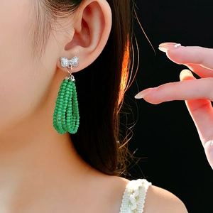 Close-up of model wearing silver bow earrings with green beaded drop pendants