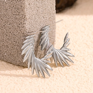 Detailed view of silver sunburst spike earrings on grey stone and warm sand background