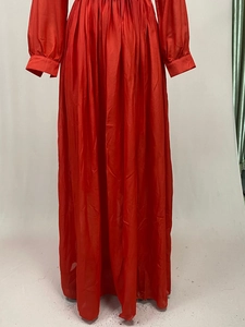 Detail of red floor-length pleated dress with long sleeves and cinched waist texture