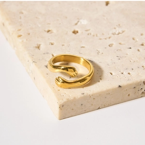 Macro detail of gold-plated embrace hands open ring on a natural stone background