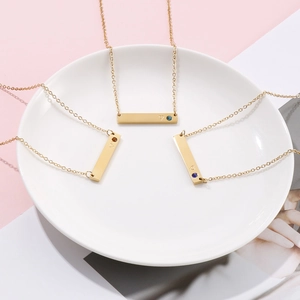 Close-up of three gold bar pendants with heart engravings and birthstones on a white plate