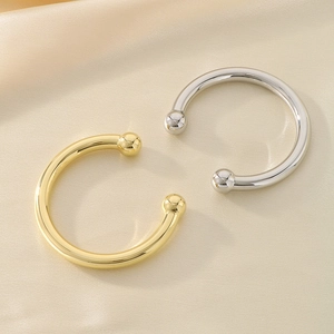 Close-up of gold and silver C-shaped bangles with metal beads on soft satin fabric