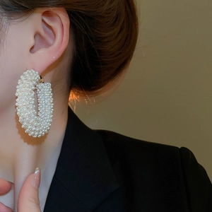 Close-up of oversized oval hoop earrings with white pearls and colorful rhinestones