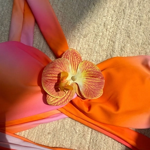Détail du haut de bikini dégradé rose-orange avec accent décoratif de fleur d'orchidée