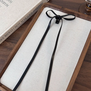 Close-up of black leather bow hair claw with long ribbons on a minimalist display