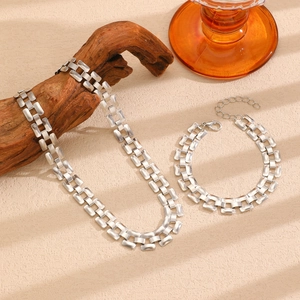 Detail of silver tank chain necklace and bracelet set on a textured beige background