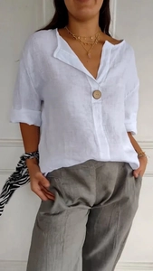 Dettaglio della maglia in cotone e lino bianco con scollo a V, bottone in legno e pantaloni grigi
